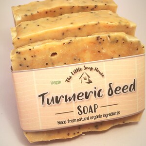 K&ouml;nnte beinhalten: Drei Seifenst&uuml;cke mit Kurkuma-Samen, hellorangefarben mit dunklen Samenflecken. Die Seife ist mit einem Etikett versehen, auf dem "Turmeric Seed Soap" und "Made from natural organic ingredients" mit dem Logo "The Little Soap House" steht.