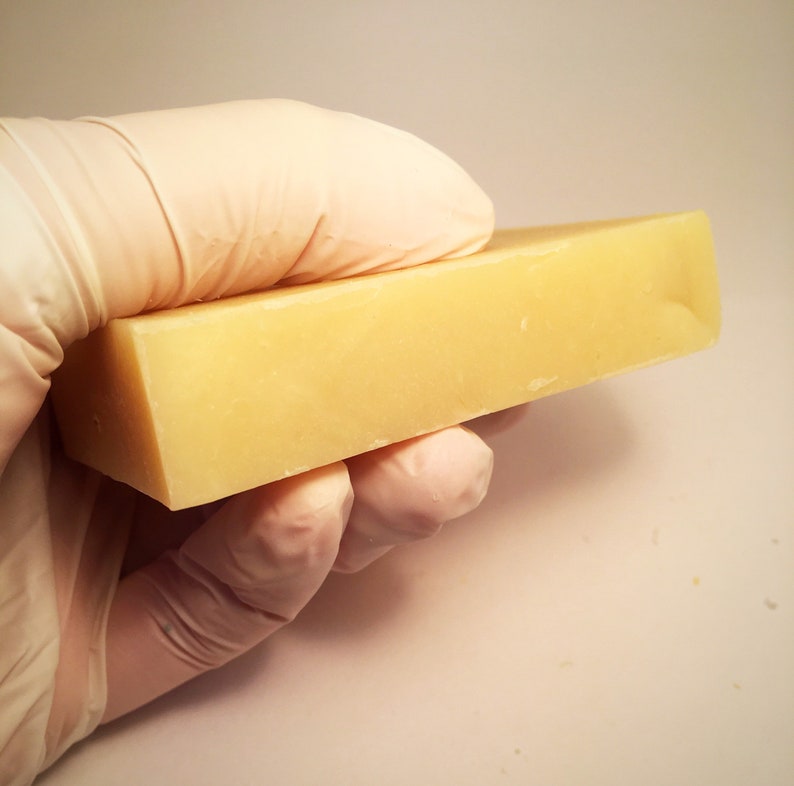 May include: A rectangular bar of pale yellow soap, held in a gloved hand.