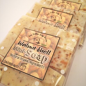 May include: Several individually wrapped mini-soaps with a light beige color and visible walnut shell pieces. Each soap is labeled with "Walnut Shell Mini-Soap" and "Natural Organic Ingredients" from The Little Soap House. The packaging states "Contains nuts".