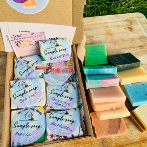 May include: An open cardboard box filled with sample soaps. The soaps are various colors and scents, including blackberry, sea salt, chocolate orange, raspberry, and mango. The box also contains a small card with tips for handmade soap.