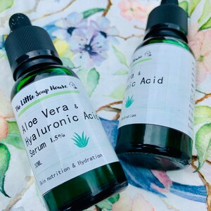 Puede incluir: Dos botellas de vidrio verde con goteros que contienen sueros para el cuidado de la piel. La botella de la izquierda est&aacute; etiquetada "The Little Soap House Aloe Vera & Hyaluronic Acid Serum 1.5% 30ML Skin nutrition & Hydration". La botella de la derecha est&aacute; etiquetada "Vera & nic Acid Hydration".