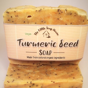 May include: Two bars of turmeric seed soap, light orange in colour with dark specks. The soap is wrapped with a label that reads "Turmeric Seed Soap" and "Made from natural organic ingredients". The label also features a small house logo.