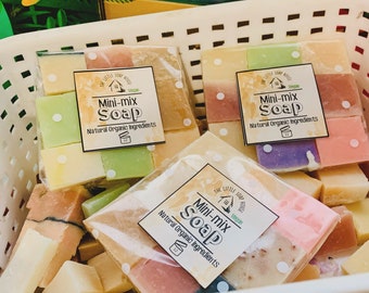 May include: A white wicker basket filled with small bars of colorful natural organic soap. The soap bars are wrapped in clear plastic and labeled "Mini-mix Soap" with the words "Vegan" and "Natural Organic Ingredients".