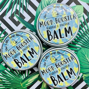 May include: Three silver tins with blue and yellow patterned labels. Each tin has the text "The Little Soap House" with a small house icon, "Mood Booster", "Natural & Organic", and "Balm".