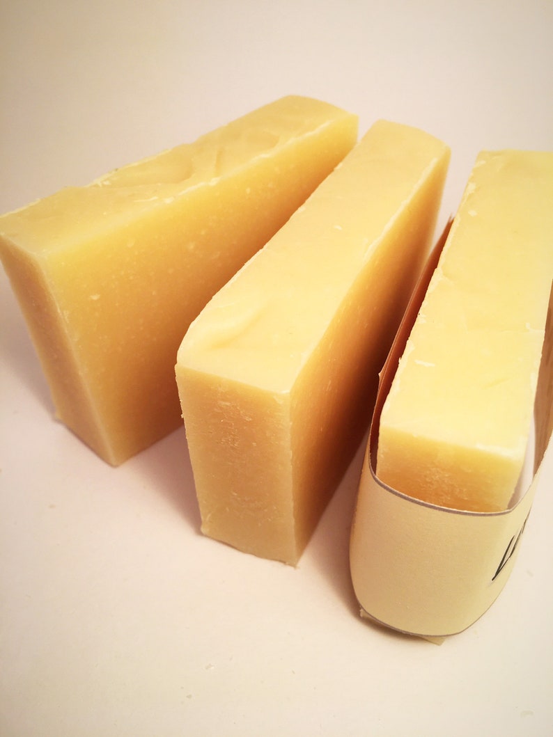 May include: Three bars of pale yellow soap, two are stacked on top of each other, and the third is wrapped in brown paper with a white label.