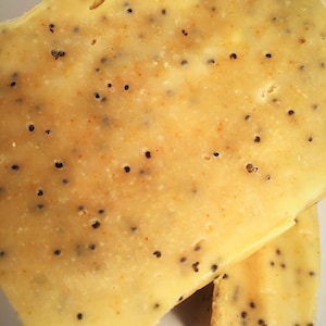 K&ouml;nnte beinhalten: Nahaufnahme von zwei K&auml;sescheiben mit hellgelber Farbe und kleinen schwarzen Samen. Der K&auml;se hat eine leicht strukturierte Oberfl&auml;che und ein paar kleine L&ouml;cher. Die Scheiben sind &uuml;bereinander gestapelt.