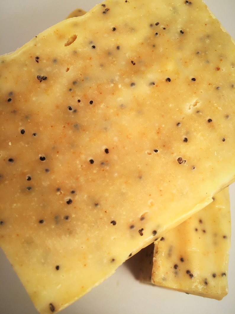 K&ouml;nnte beinhalten: Nahaufnahme von zwei K&auml;sescheiben mit hellgelber Farbe und kleinen schwarzen Samen. Der K&auml;se hat eine leicht strukturierte Oberfl&auml;che und ein paar kleine L&ouml;cher. Die Scheiben sind &uuml;bereinander gestapelt.