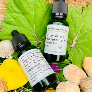 Puede incluir: Dos botellas de vidrio verde con goteros, etiquetadas con "The Little Soap House Aloe Vera & Hyaluronic Acid Serum 1.5%". Las botellas est&aacute;n sobre un lecho de hierba verde y conchas marinas. El texto en las botellas dice "Skin nutrition & Hydration" e "Ingredientes: Aloe Vera Liquid, Hyaluronic Acid 1.5% DL-Panthenol Pro Vitamin B5, Vegetable Glycerine, Rose & Lime Essential Oil."
