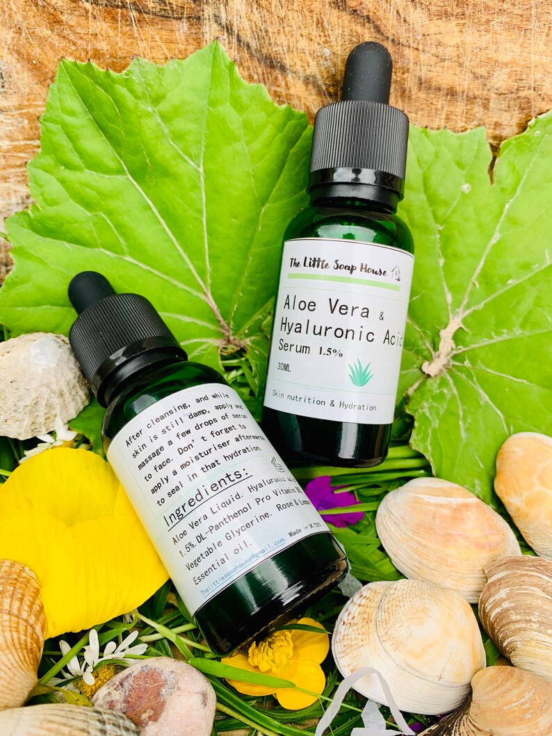 Puede incluir: Dos botellas de vidrio verde con goteros, etiquetadas con "The Little Soap House Aloe Vera & Hyaluronic Acid Serum 1.5%". Las botellas est&aacute;n sobre un lecho de hierba verde y conchas marinas. El texto en las botellas dice "Skin nutrition & Hydration" e "Ingredientes: Aloe Vera Liquid, Hyaluronic Acid 1.5% DL-Panthenol Pro Vitamin B5, Vegetable Glycerine, Rose & Lime Essential Oil."