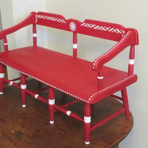 May include: A red wooden bench with white painted accents and a white dotted trim. The bench has a simple design with a curved back and armrests.