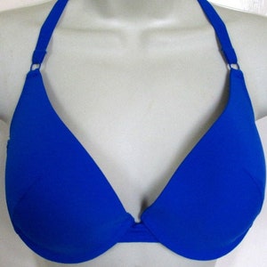 May include: A solid royal blue bikini top featuring a halter neck design with thin straps that connect to the cups via small circular rings. The garment has a deep V-neckline and a structured underwire construction for support and shape.