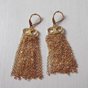 May include: A pair of gold-colored tassel earrings. Each earring features a rectangular top with a decorative design and a cascade of delicate gold chains. The earrings have a lever-back closure.