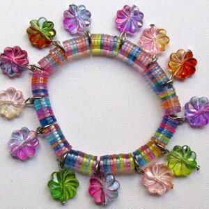 May include: A colourful bracelet made of stacked, iridescent, round beads with flower-shaped charms hanging from it. The charms are made of iridescent plastic and come in a variety of colours, including pink, purple, blue, green, and orange.