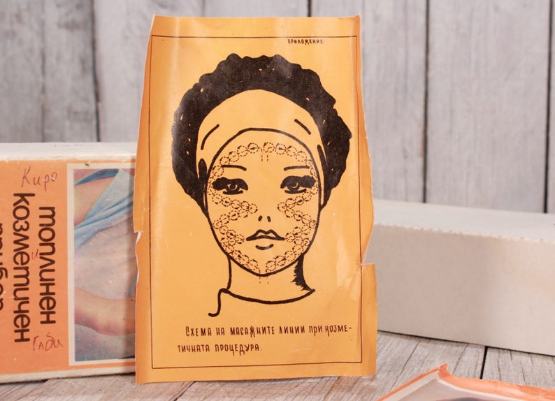 May include: Vintage orange paper with a black illustration of a woman's face, featuring a headband and dotted patterns on the face. Text in Russian is visible on the paper and a box in the background. The image suggests a skincare or beauty product.