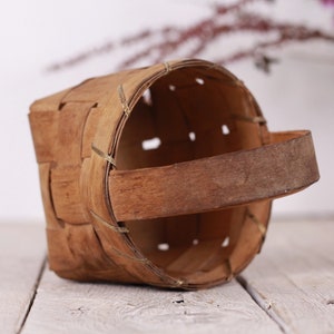Puede incluir: Una peque&ntilde;a cesta artesanal hecha de tiras de madera tejidas. La cesta tiene forma rectangular con la parte superior redondeada y un asa resistente. Los tonos naturales de la madera y el dise&ntilde;o sencillo le dan un aspecto r&uacute;stico y vintage.