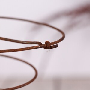 May include: Close-up of a rusty metal spring, showcasing its spiral form and the connection point where the wire is joined. The aged appearance suggests vintage or antique origins. The spring's color is a warm, earthy brown.