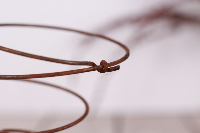 May include: Close-up of a rusty metal spring, showcasing its spiral form and the connection point where the wire is joined. The aged appearance suggests vintage or antique origins. The spring's color is a warm, earthy brown.