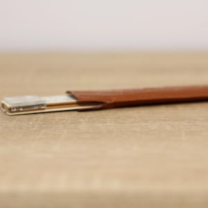 May include: A brown leather case with a silver and gold ruler inside.