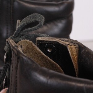 May include: Close-up of the inside of a black leather boot with green laces. The boot has a brown leather lining and a metal eyelet.