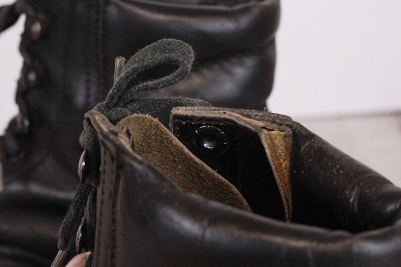 May include: Close-up of the inside of a black leather boot with green laces. The boot has a brown leather lining and a metal eyelet.