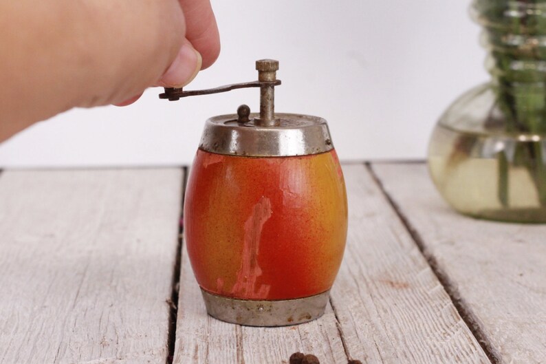 May include: A vintage pepper mill with a barrel-shaped body. The wooden body transitions from yellow to orange. It has a silver-colored top and bottom with a crank for grinding. A classic kitchen tool.