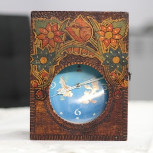 May include: A wooden clock with a blue face and white hands. The clock is decorated with painted flowers and leaves in shades of brown, orange, and green.