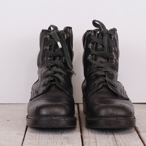 May include: A pair of black leather lace-up boots with green laces. The boots have a worn look and are sitting on a wooden surface.