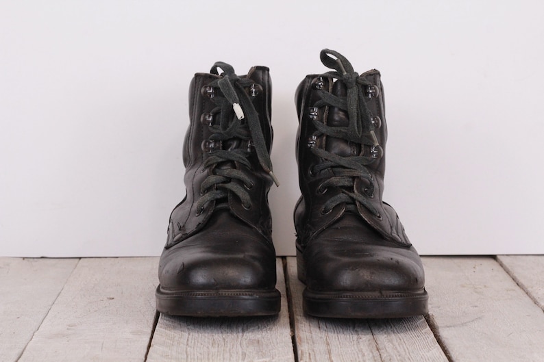 May include: A pair of black leather lace-up boots with green laces. The boots have a worn look and are sitting on a wooden surface.