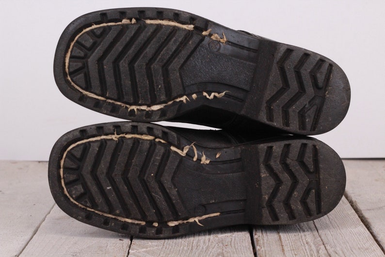 May include: Close-up of the bottom of a pair of black leather boots with a textured rubber sole.