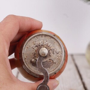May include: A vintage apple-shaped pencil sharpener with a metal crank and a silver-colored metal base. The sharpener has an orange and yellow body with a slightly worn appearance. The crank is in the down position.