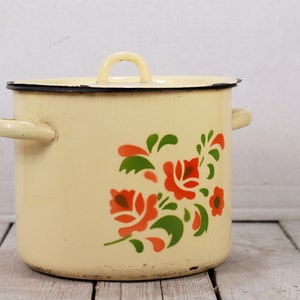 Könnte beinhalten: Ein vintage Emailletopf in Cremefarbe mit einem floralen Design in Orange- und Grüntönen. Der Topf hat zwei Griffe und einen Deckel.