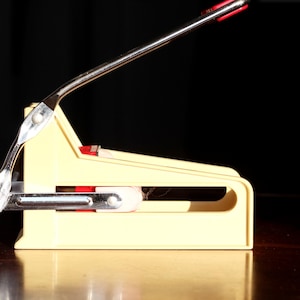 May include: A white plastic french fry cutter with a silver metal handle and a red lever. The cutter is on a dark brown surface.