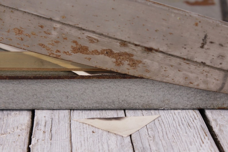 May include: A weathered, gray wooden structure with visible rust and a triangular piece of paper. The wood has a distressed appearance, suggesting age or exposure to the elements. The paper is a light color with a dark stain.