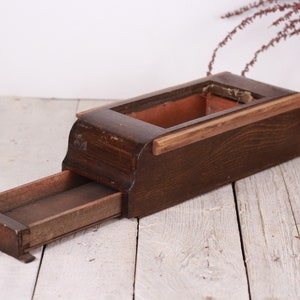 Op de afbeelding: Een vintage houten kist met een uitschuifbare lade. De kist is rechthoekig, donkerbruin van kleur, met een lichtere houten rand rond de bovenste opening. De lade is open.