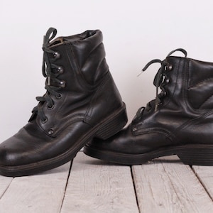 May include: A pair of black leather lace-up boots with a chunky sole. The boots have a slightly distressed look and are tied with green laces.