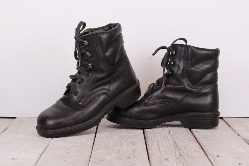 May include: A pair of black leather lace-up boots with a chunky sole. The boots have a slightly distressed look and are tied with green laces.