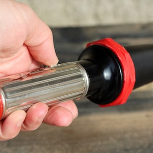 May include: A silver flashlight with a red and black plastic end cap. The flashlight has a ribbed body and a red cap with a white button.