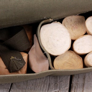 K&ouml;nnte beinhalten: Ge&ouml;ffnete olivgr&uuml;ne Canvas-Tasche, gef&uuml;llt mit mehreren Rollen cremefarbenen Materials. Die Tasche enth&auml;lt auch kleine braune P&auml;ckchen und einen dunkelgr&uuml;nen Riemen. Der Inhalt ist sichtbar.