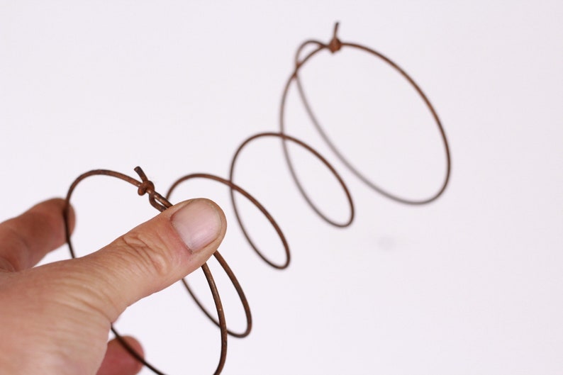 May include: A brown metal spring held by a hand against a white background. The spring is coiled and has a series of circular loops. The metal appears to be aged or weathered, giving it a rustic appearance.