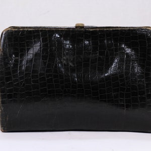 May include: A black leather clutch purse with a crocodile embossed pattern. The purse has a gold metal clasp.