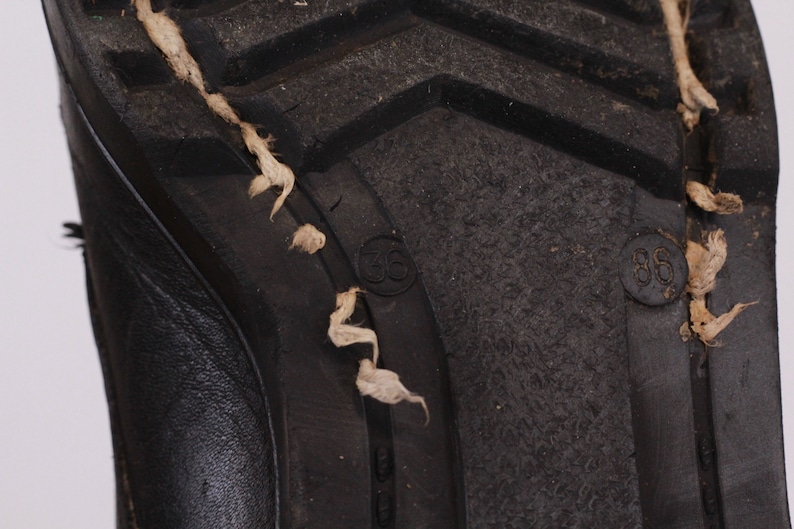 May include: Close-up of the bottom of a black leather boot with a rubber sole. The sole has the numbers "36" and "38" printed on it.