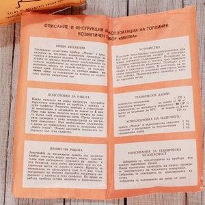 May include: Open orange pamphlet with Bulgarian text, detailing instructions for a cosmetic device. The pamphlet is on a light wood surface, with a matching orange package visible.