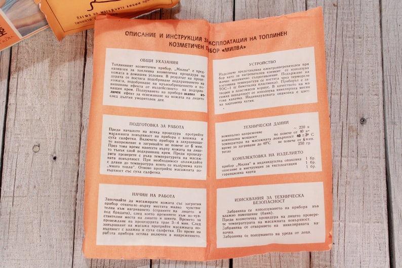 May include: Open orange pamphlet with Bulgarian text, detailing instructions for a cosmetic device. The pamphlet is on a light wood surface, with a matching orange package visible.