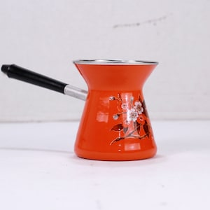 May include: Orange and white enamel coffee pot with a black handle. The pot has a floral design.