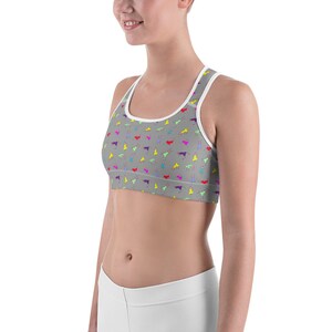 May include: Gray sports bra with a white trim and a colorful llama pattern. The llamas are in various colors, including yellow, purple, and blue. The bra is designed for athletic activities.