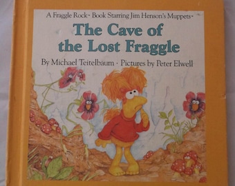 May include: A vintage children's book titled "The Cave of the Lost Fraggle" featuring a cartoon Fraggle Rock character. The cover is yellow with the title in blue and the author's name. The book is a collectible item.