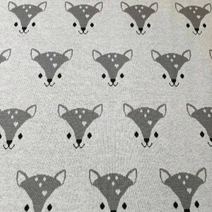 Könnte beinhalten: Ein weißer gestrickter Stoff mit einem sich wiederholenden Muster aus grauen Hirschgesichtern. Die Hirsche haben schwarze Augen und Nasen und weiße Flecken.