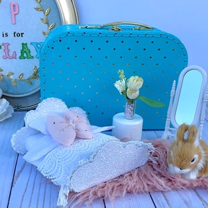Puede incluir: Una escena caprichosa con una maleta azul con lunares dorados, un lazo blanco y rosa y un espejo pequeño. Un letrero enmarcado dice "P is for PLAY". Un conejito esponjoso está sentado en una alfombra rosa.