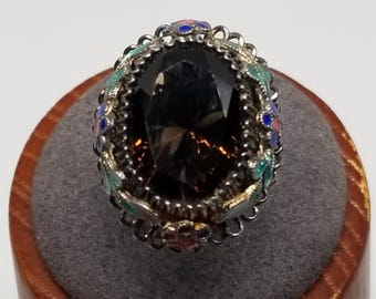May include: A silver ring with a large, dark brown gemstone surrounded by a decorative filigree setting. The setting is accented with colorful enamel in shades of blue, green, and red.