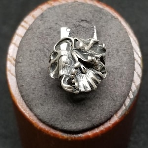 May include: A silver bead charm featuring a detailed, three-dimensional floral design with layered petals and curved leaves. The metal has a polished finish with darkened recessed areas to highlight the intricate textures of the organic flower shape.